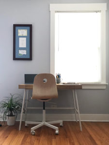 chair and desk in a blue room with framed art and a window in the background